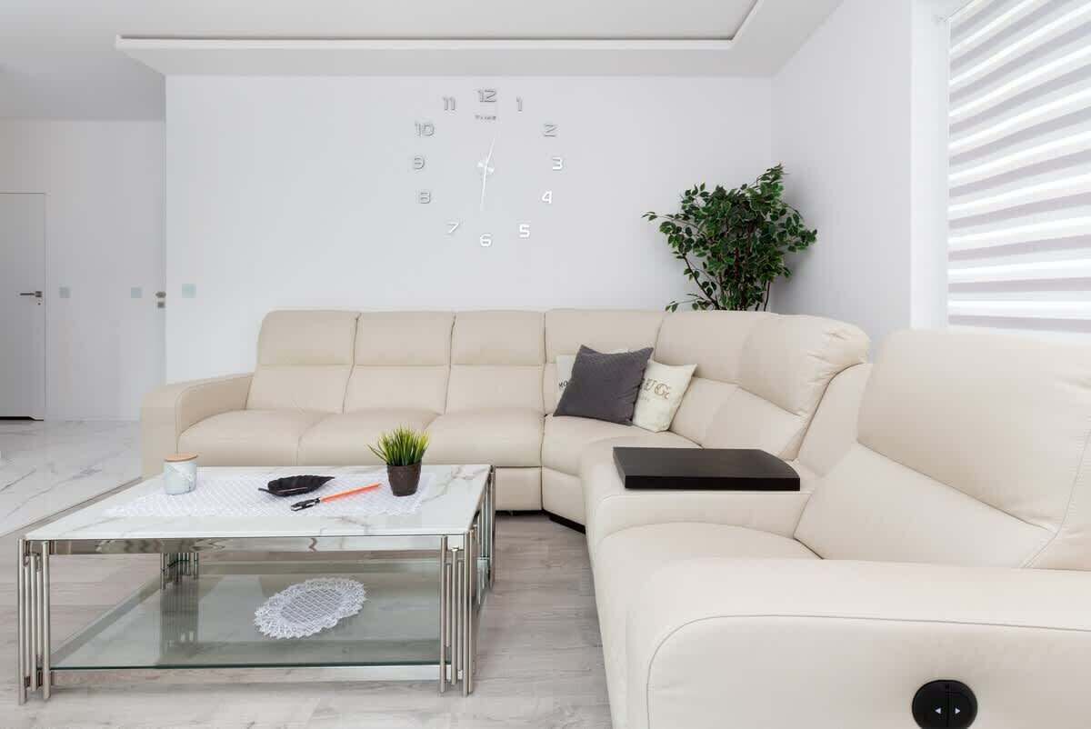 A bright and elegant living room featuring a cream leather sofa, a glass coffee table, and modern decor.
