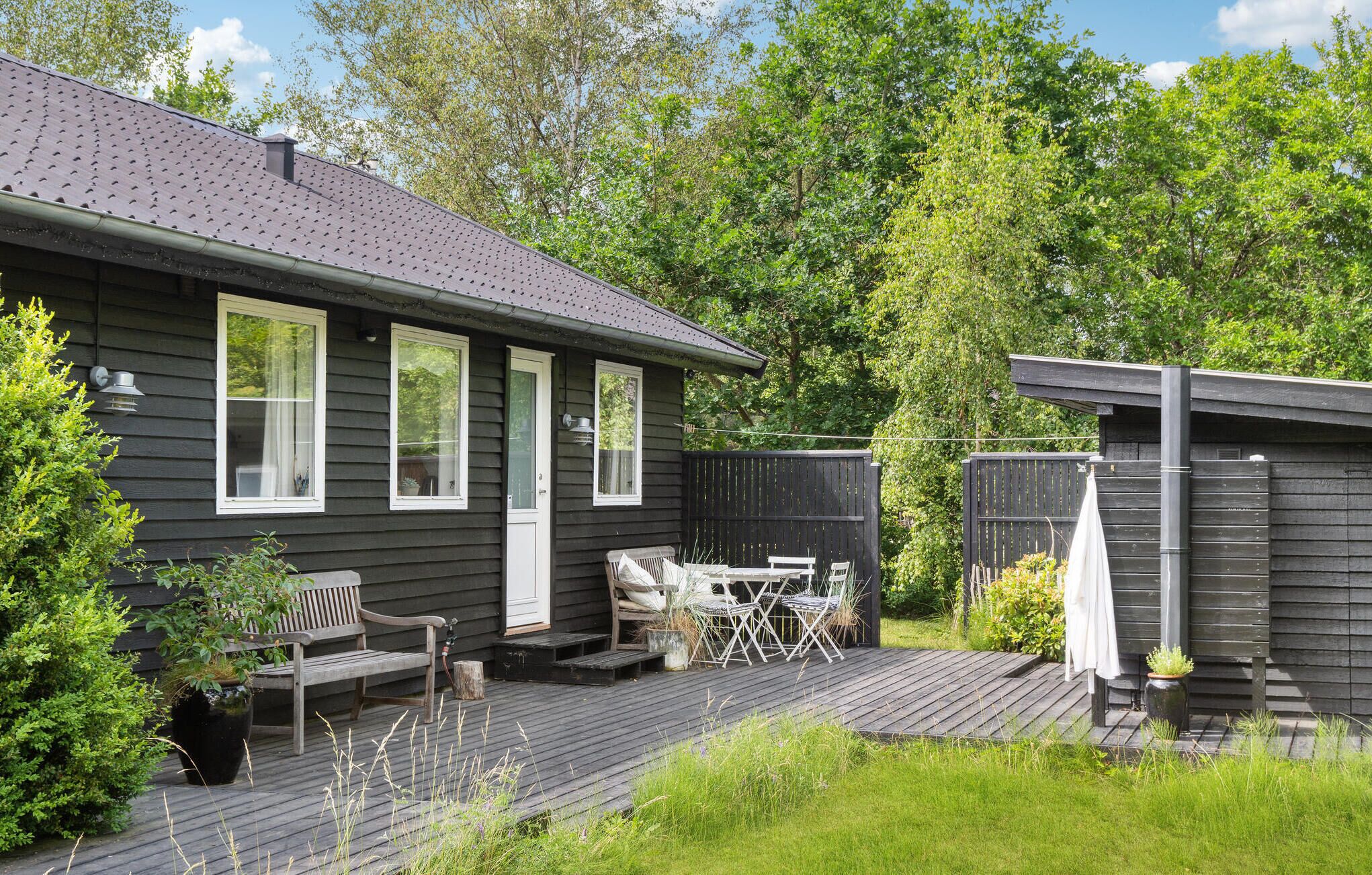 A house with a deck, a patio with outdoor furniture, and a fenced garden area.