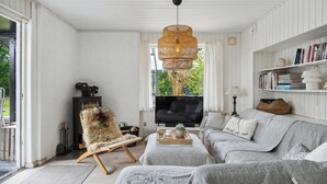 Ett vardagsrum med en soffa, en fåtölj, en tv, en bokhylla och ett stort fönster.