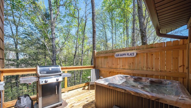 Eine Holzterrasse mit Grill, Whirlpool und einem Schild mit der Aufschrift 'Our Happy Place'.