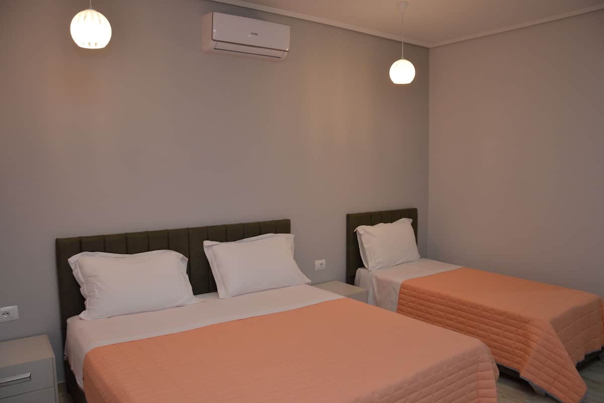 Une chambre d’hôtel avec deux lits simples, une table de chevet, un appareil de climatisation et deux lampes suspendues.