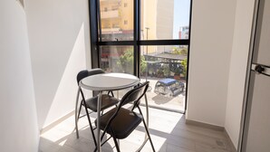 A small balcony with a table and chairs, overlooking a street with parked vehicles and buildings. - Hotel Beler (Vlorë)