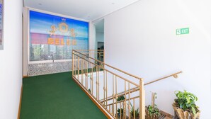 A staircase with a green carpet, a wooden railing, and potted plants. - Hotel Beler (Vlorë)