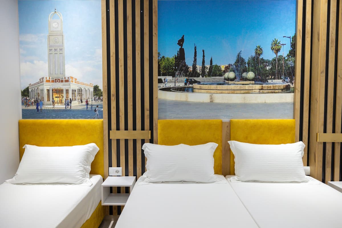 Une chambre d’hôtel avec un lit, une table de chevet et une grande fenêtre ornée d’une fresque représentant un paysage urbain.