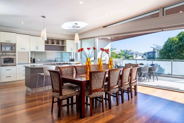 A modern kitchen with a dining area, featuring a large island, wooden chairs, and a view of the outdoors.