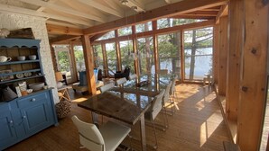 Une cabine spacieuse dotée d’une grande table à manger, de planchers en bois et de grandes fenêtres offrant une vue sur le lac.