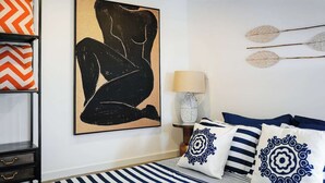 Een moderne slaapkamer met een groot abstract schilderij, gestreept beddengoed en decoratieve kussens.