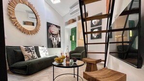 Een moderne woonkamer met een ronde salontafel, een groene bank, een houten trapje en een grote spiegel aan de muur.