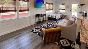 A cozy living room with a sofa, a patterned rug, and a television on the wall. - Cozy home sleeps 4 & just a few steps to the beach & Linens Included! (Edisto Island)