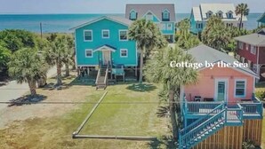 A coastal cottage with a staircase leading to the entrance, surrounded by palm trees and a view of the sea. - Cozy home sleeps 4 & just a few steps to the beach & Linens Included! (Edisto Island)