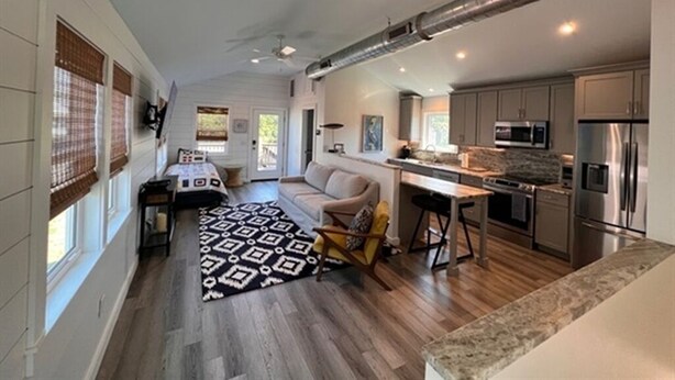A spacious living area with a sofa, a coffee table, and a patterned rug. There is a kitchen with modern appliances and a dining area with a table and chairs. - Cozy home sleeps 4 & just a few steps to the beach & Linens Included! (Edisto Island)