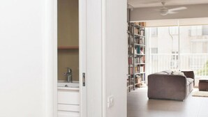 An open doorway leading to a living area with a sofa, a bookshelf, and a view of the outdoors. - Spacious & Stylish 3BR Apt w Beautiful Street View (Tel Aviv)