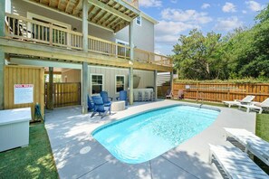 Una casa de dos pisos con piscina en el patio trasero, mobiliario exterior y una terraza de madera.