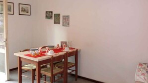 Uma sala de jantar com mesa posta para quatro pessoas, luminária pendente e quadros nas paredes.