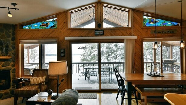 Een gezellig interieur met een stenen open haard, houten wanden en grote ramen met uitzicht op een besneeuwd terras.