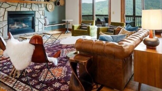 Ein geräumiges Wohnzimmer mit Kamin aus Stein, Ledersofa und großen Fenstern mit Blick ins Freie.