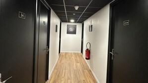 A corridor with wooden flooring, dark walls, and doors marked with room numbers. - Le Costellan (Dagneux)