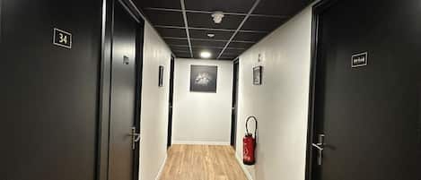 Un pasillo con suelo de madera, paredes oscuras y puertas numeradas.