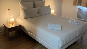 A neatly made bed with white linens and pillows, a bedside lamp, and a rolled towel on the bed. - Le Costellan (Dagneux)