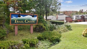Un panneau indiquant « Trail Creek », avec une représentation graphique d’une montagne, entouré de verdure et d’un bâtiment doté d’un toit rouge.