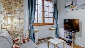 A living room with a stone wall, a television, a small table, and a sofa with patterned cushions. - Pause Café (Annecy)