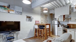 A modern kitchen with a large TV, wooden stools, a stone accent wall, and stainless steel appliances. - Pause Café (Annecy)
