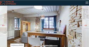 Enjoy meals in the dining area with a wooden table and chairs, surrounded by a stone wall and large window with curtains.