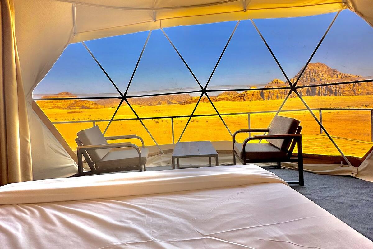 A tented room with a bed, two chairs, and a small table.