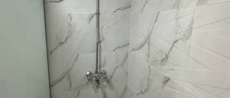 A bathroom with marble walls and a shower.