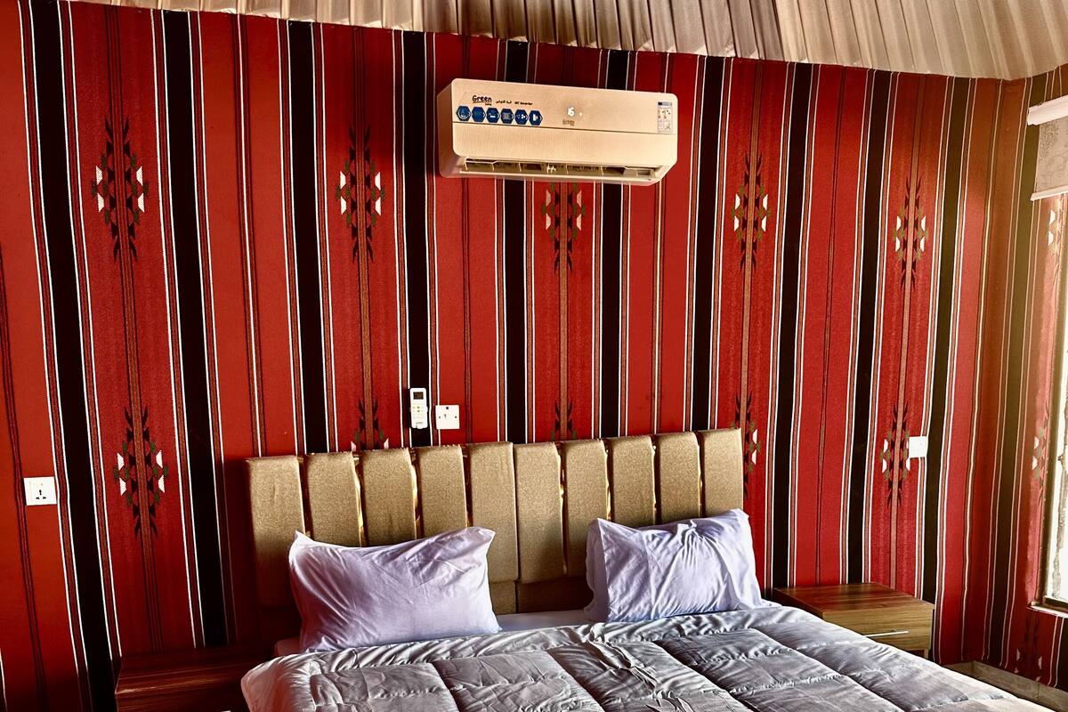 A double bed with a headboard, a bedside table, and a wall-mounted air conditioner.