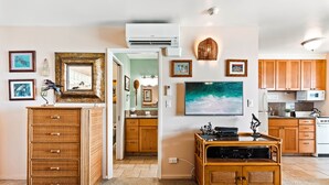 Una sala moderna con un televisor de pantalla plana grande, muebles de mimbre y una zona de cocina con armarios de madera.