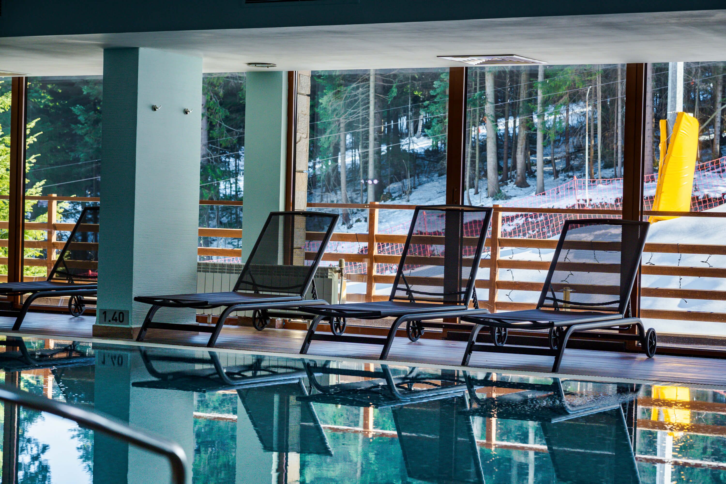 A pool area with lounge chairs and a view of a snowy forest through large windows.