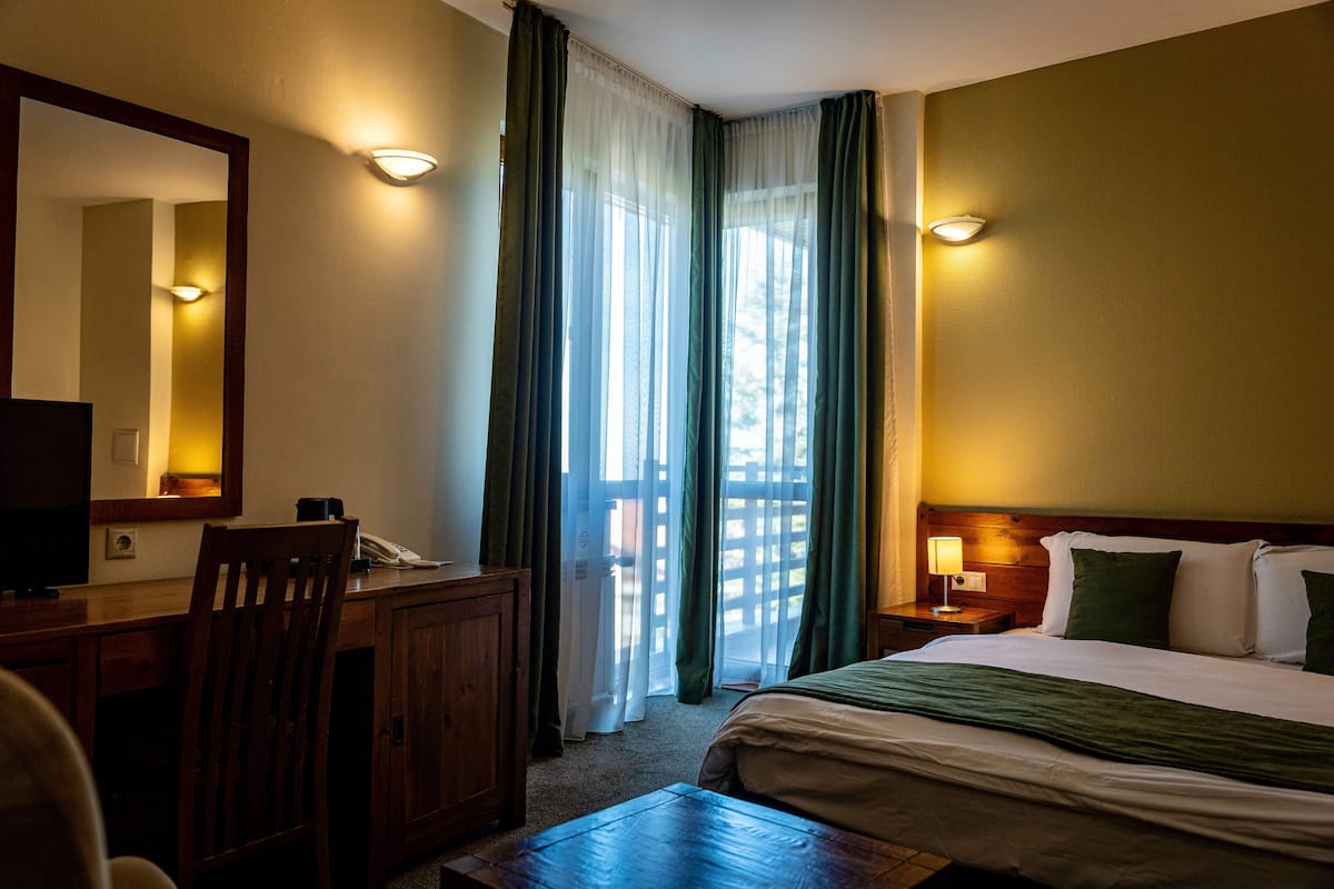 Una habitación de hotel con cama, escritorio, silla y un ventanal con cortinas.