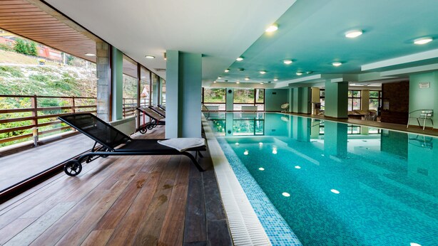 Una piscina interior con cubierta de madera, sillas de descanso y vistas al exterior.