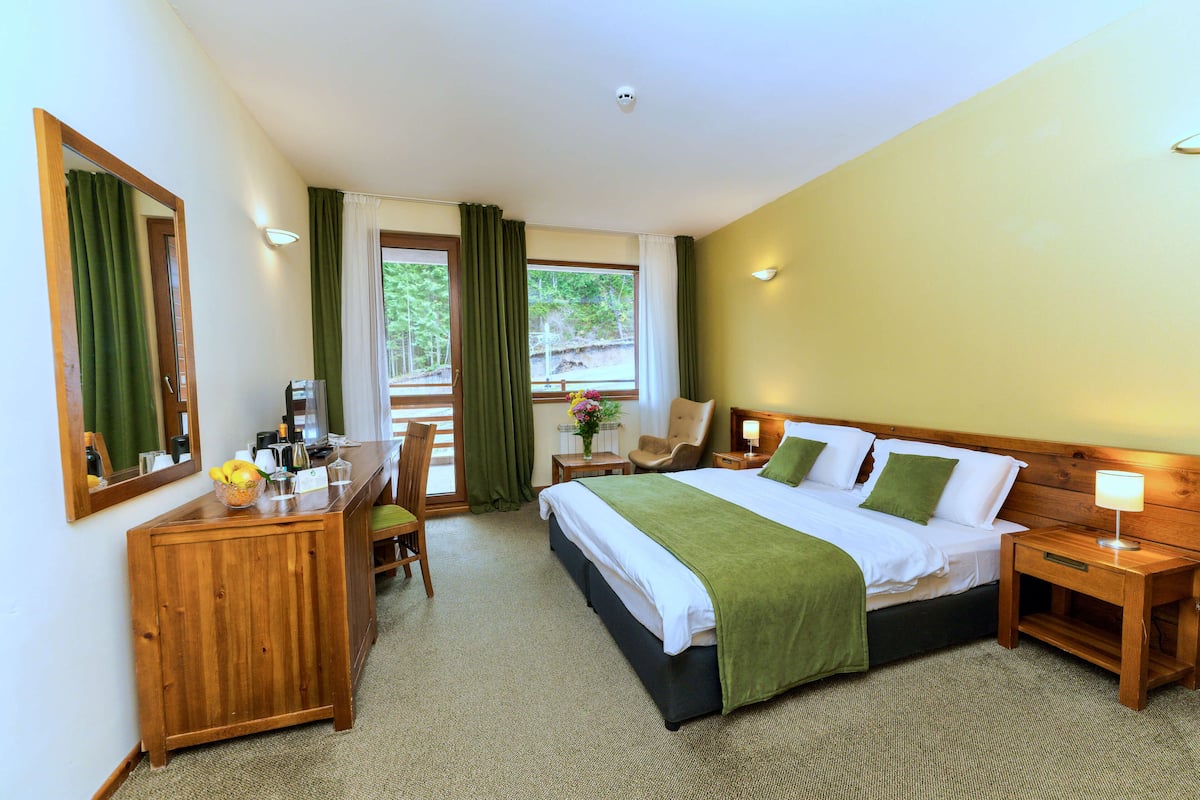 Habitación de hotel con cama, escritorio, silla, mesita de noche y ventana con cortinas.