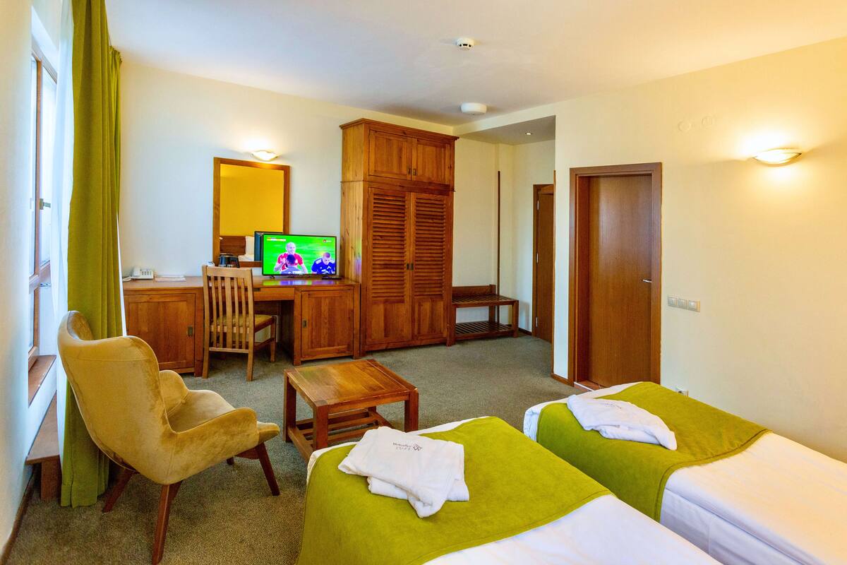 Una habitación de hotel con dos camas, un escritorio de madera, un televisor y una silla.