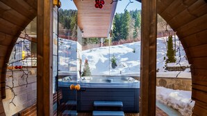 Un jacuzzi con bancos y escalones de madera, rodeado por una terraza de madera y un paisaje cubierto de nieve.