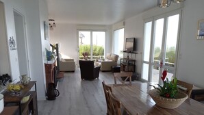A spacious living area with a wooden dining table, comfortable seating, and large windows. -  The house right on the water with direct access to the beach. (Ouistreham)