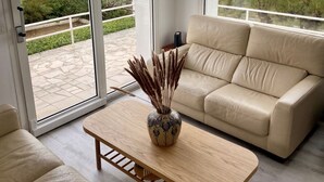 A modern living room with a beige sofa, a wooden coffee table, and a vase with dried plants. Large glass doors lead to a patio with a view of the beach and the sea. -  The house right on the water with direct access to the beach. (Ouistreham)