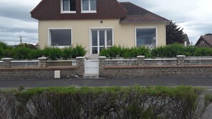 A two-story house with a pitched roof, large windows, and a stone wall in front. -  The house right on the water with direct access to the beach. (Ouistreham)