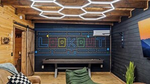 A room with a wooden ceiling, a neon sign spelling 'LOOKOUT,' a bench, a green bean bag, and a plant. - Secluded cabin w views! Game Room & FREE TIX! (Sevierville)