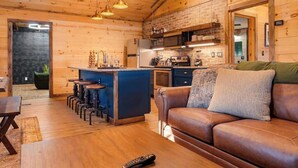 A cozy cabin interior with a wooden ceiling, a kitchen area with a bar counter, and a leather sofa. - Secluded cabin w views! Game Room & FREE TIX! (Sevierville)