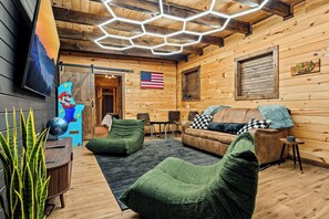 L’intérieur d’un chalet accueillant, avec un revêtement mural en bois, un canapé, un fauteuil vert, une petite table et un drapeau accroché au mur.