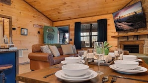 A wooden interior with a dining table set for four, a leather sofa, and a fireplace. - Secluded cabin w views! Game Room & FREE TIX! (Sevierville)