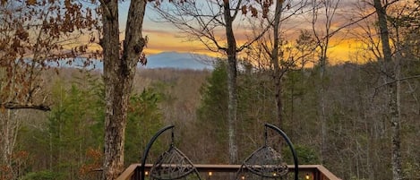 A wooden deck with two black wire chairs facing a forested landscape.