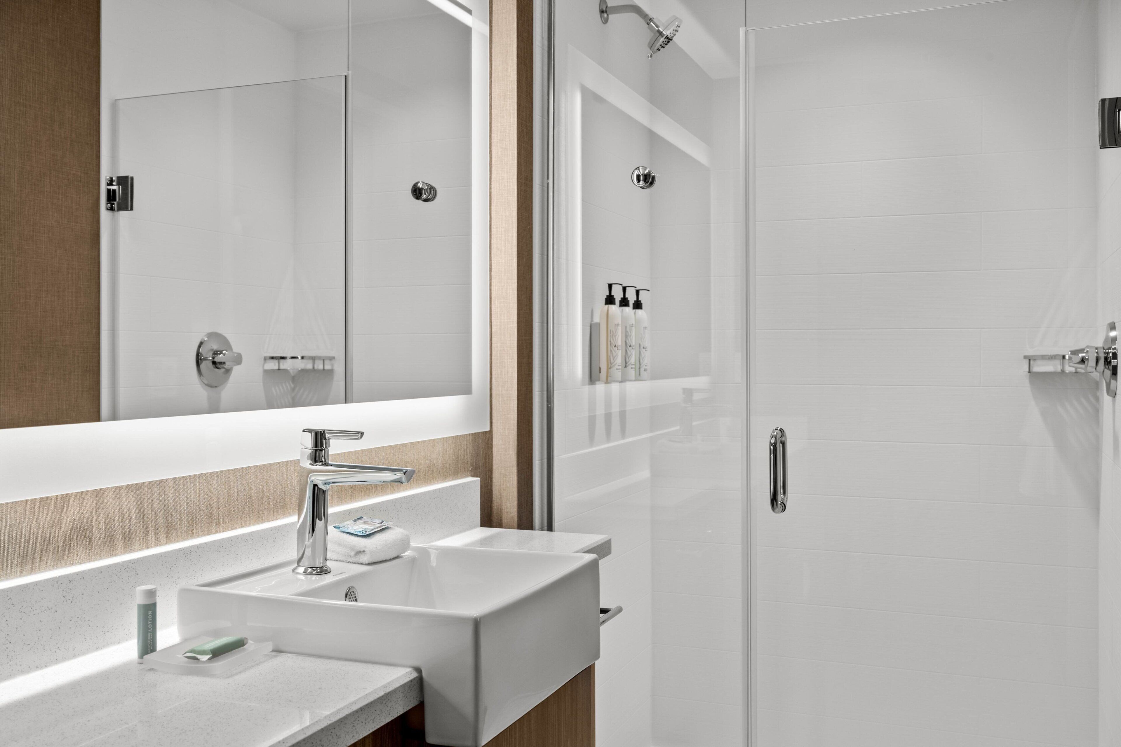 A modern bathroom with a large mirror, two sinks, and a shower.