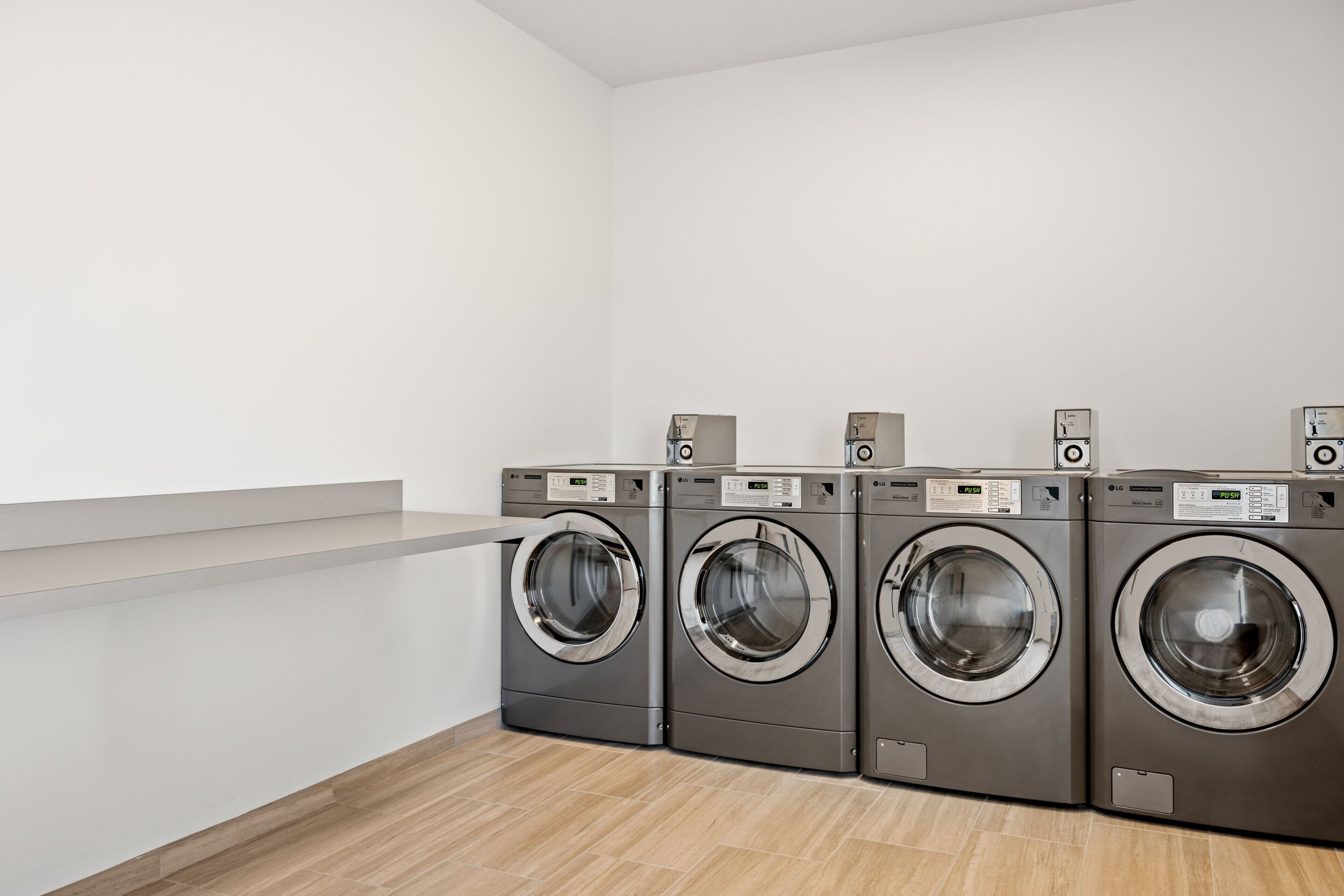 A laundry room with four front-loading washing machines and a white wall.