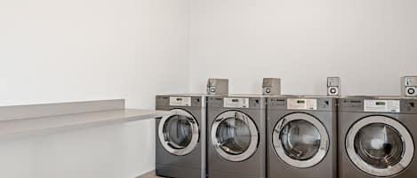A laundry room with four front-loading washing machines and a white wall.