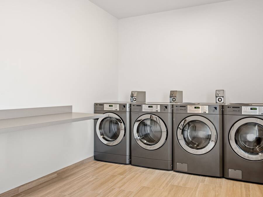 A laundry room with four front-loading washing machines and a white wall.