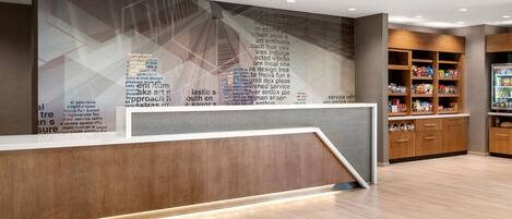A modern reception area with a wooden reception desk, a wall with text, and a snack bar with shelves.